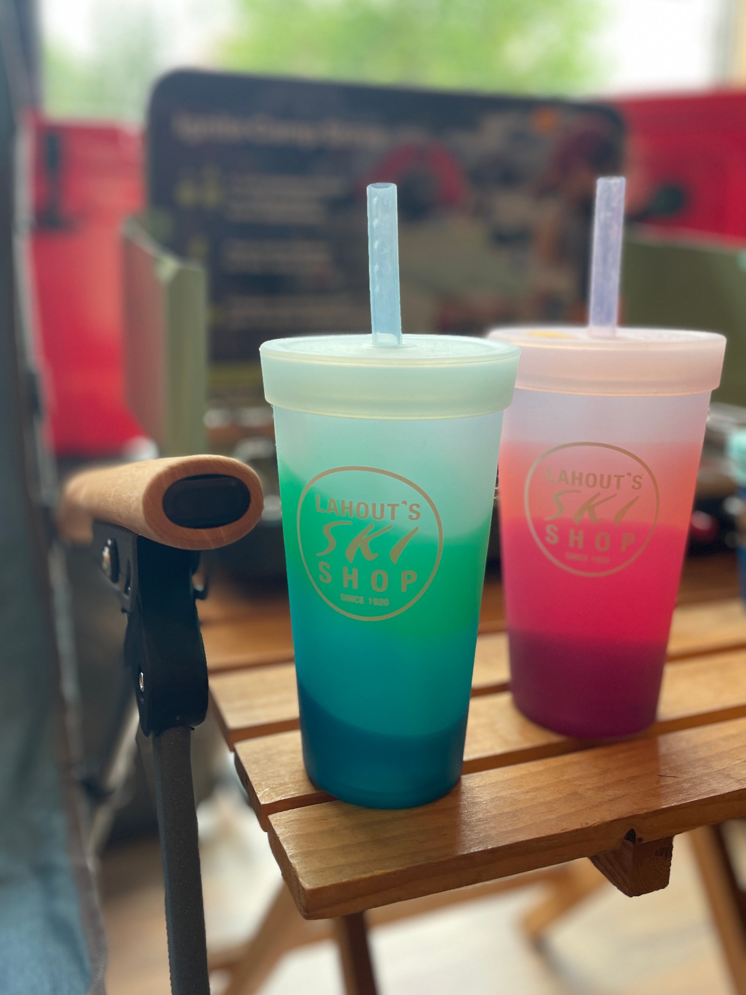 Silipint 22oz Silicone Tumbler with straw in color Desert Sun (pink hues) & Mountain Air (Blue hues) sitting together on fold up wooden camp table